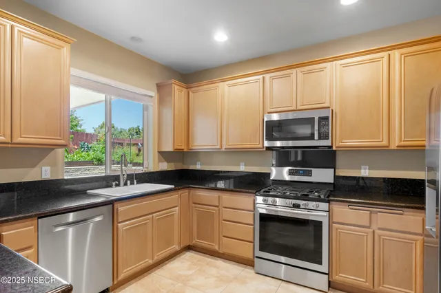 a kitchen with granite countertop a sink cabinets stainless steel appliances and a window