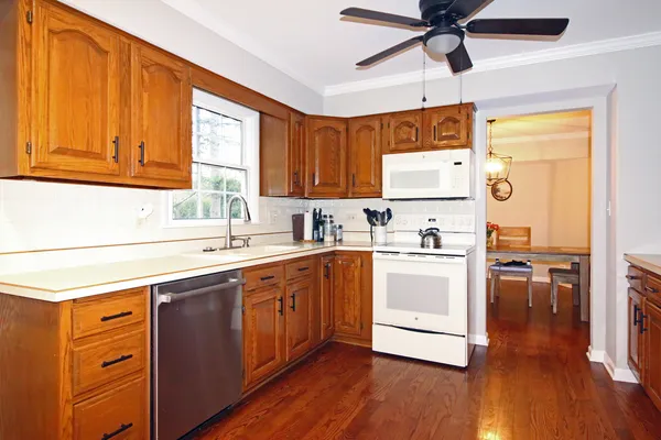 a kitchen with stainless steel appliances a stove a sink and white cabinets with wooden floor next to windows