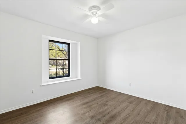an empty room with wooden floor ceiling fan and windows