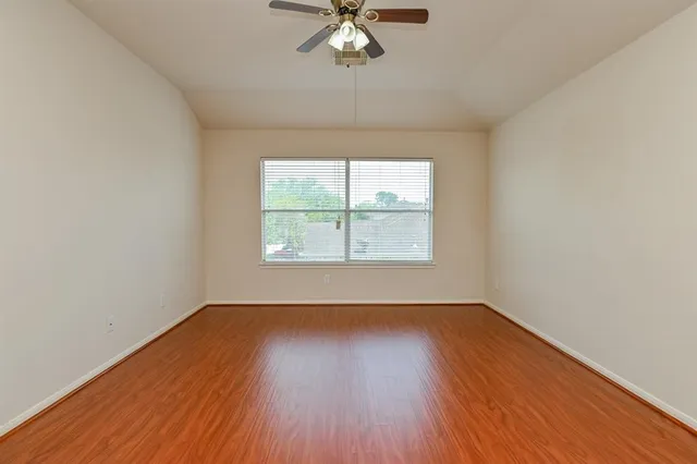 an empty room with wooden floor chandelier fan and windows