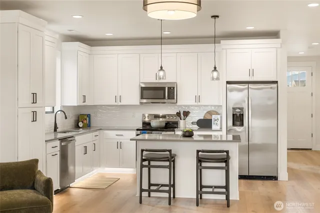 a kitchen with stainless steel appliances granite countertop a stove a sink a refrigerator and a dining table with wooden floor