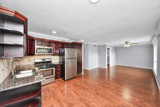 a kitchen with granite countertop a refrigerator a stove a sink and white cabinets with wooden floor