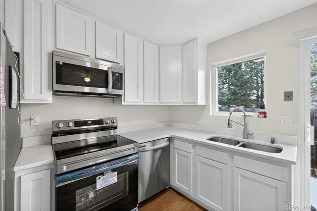 a kitchen with stainless steel appliances granite countertop white cabinets a microwave oven a sink and dishwasher with wooden floor