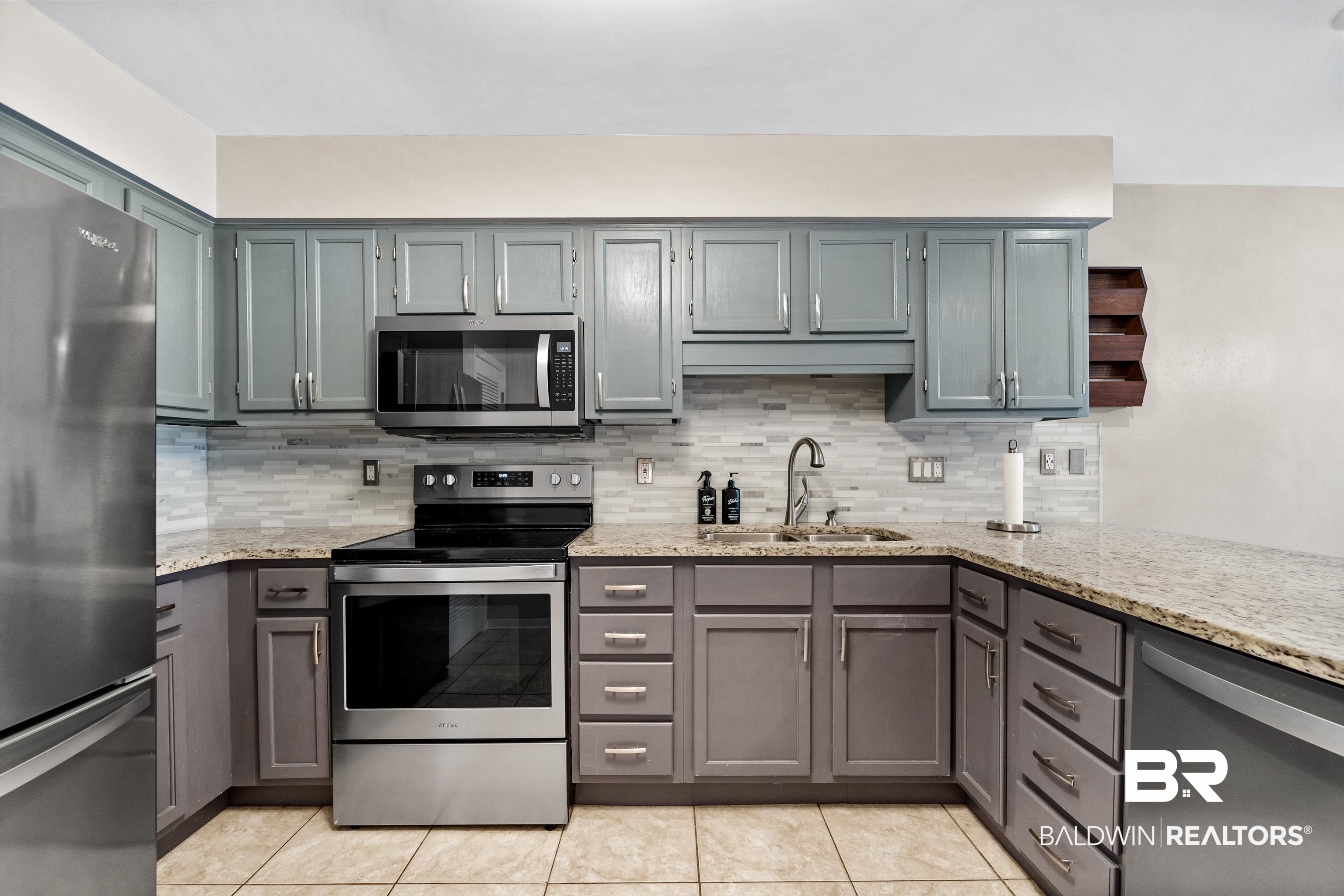 1701 Regency Road, Unit 111 Gulf Shores, AL 36542 - Photo 12 of 29 Kitchen featuring gray cabinetry, light stone countertops, appliances with stainless steel finishes, and sink