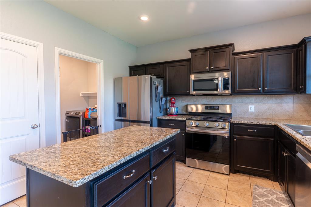 753 Rutherford Drive Crowley, TX 76036 - Photo 10 of 26 Kitchen featuring dark wood cabinetry, stainless steel appliances, a tile backsplash, and granite countertops