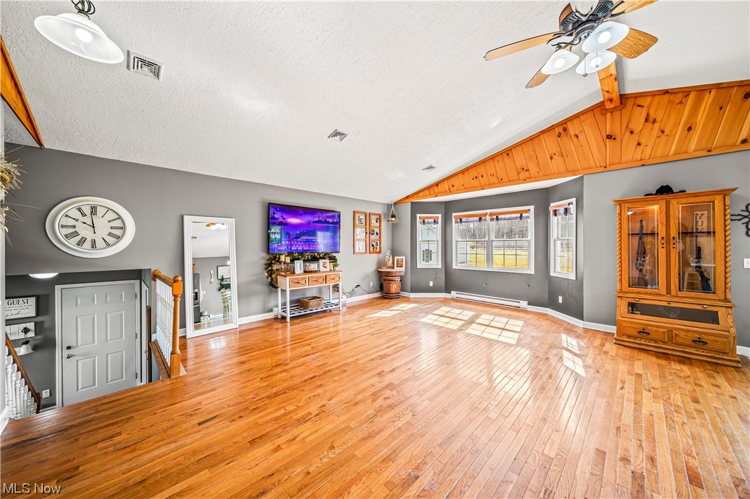 7290 Turner Road Pierpont, OH 44082 - Photo 7 of 36 Unfurnished living room featuring a baseboard radiator, ceiling fan, lofted ceiling with beams, and light hardwood / wood-style flooring