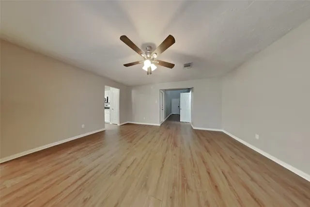 a view of an empty room with wooden floor and a ceiling fan