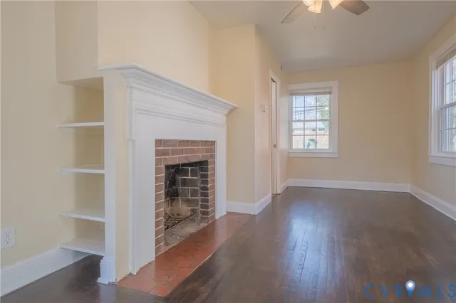 an empty room with wooden floor fireplace and windows