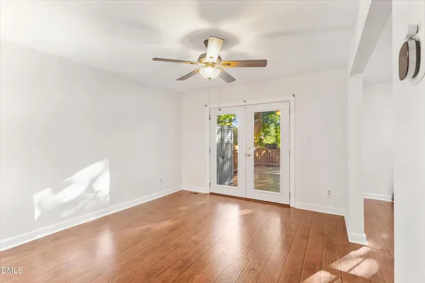 an empty room with wooden floor chandelier fan and windows