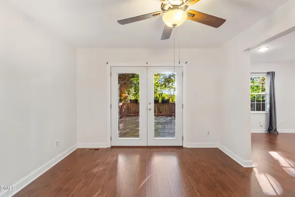 an empty room with wooden floor chandelier fan and windows