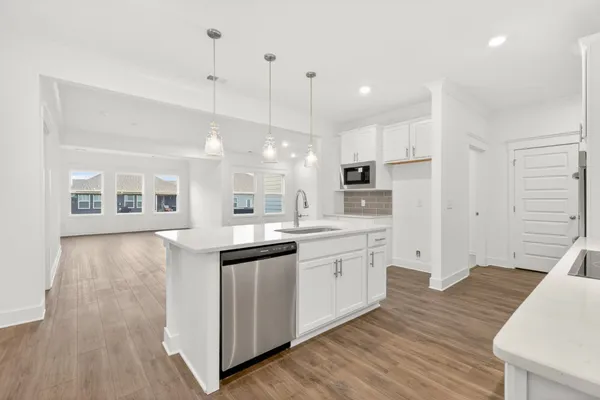 a kitchen with stainless steel appliances granite countertop a sink a microwave oven a refrigerator and white cabinets with wooden floor