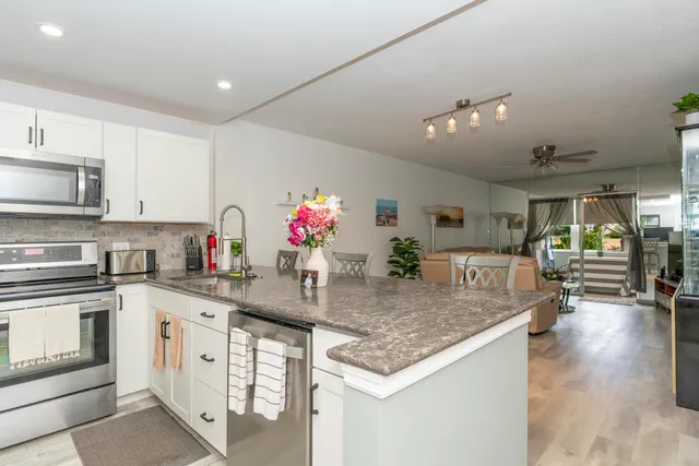 a kitchen with stainless steel appliances granite countertop a sink dishwasher a stove and white cabinets with wooden floor