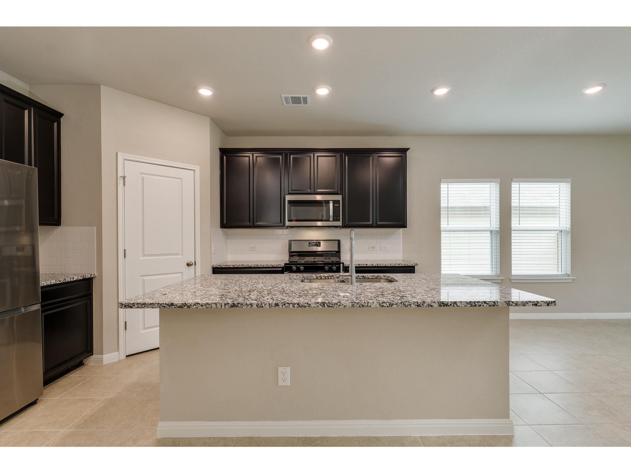 111 Grapefruit Road Hutto, TX 78634 - Photo 11 of 39 Kitchen featuring appliances with stainless steel finishes, a sink, light stone counters, a center island with sink, and recessed lighting