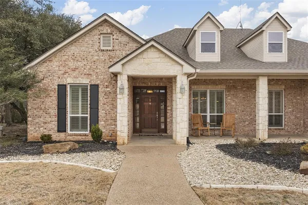 a view of a house with small yard plants and large tree