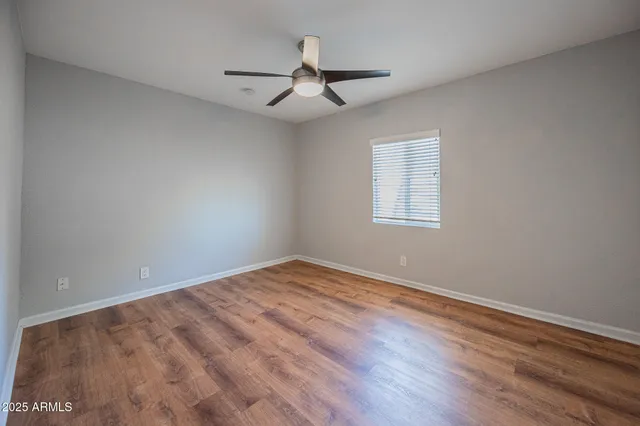 an empty room with wooden floor ceiling fan and windows