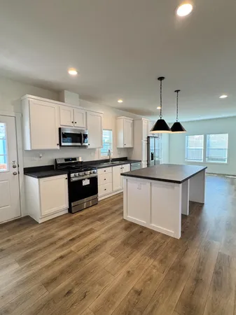 a large kitchen with kitchen island a stove a sink a refrigerator and white cabinets with wooden floor