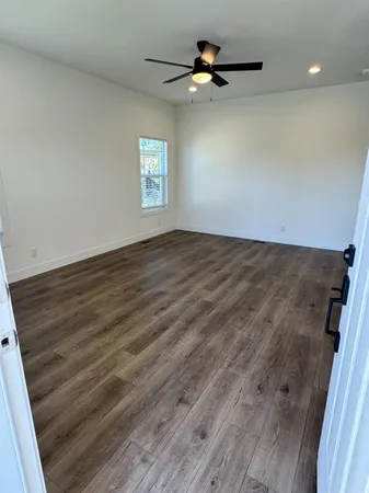 an empty room with wooden floor fan and windows
