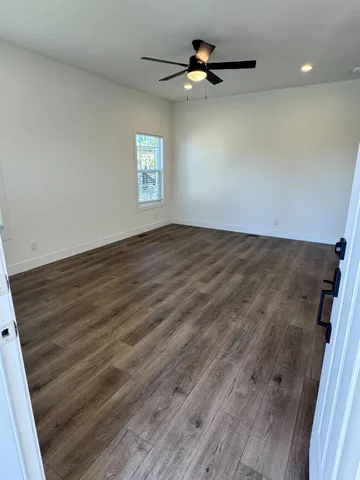 an empty room with wooden floor fan and windows