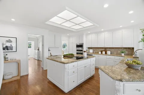 a kitchen with a stove a sink a refrigerator and white cabinets with wooden floor