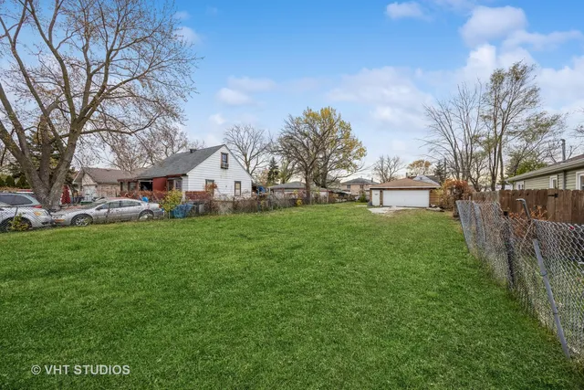 a view of a white house in front of a big yard with plants and large trees