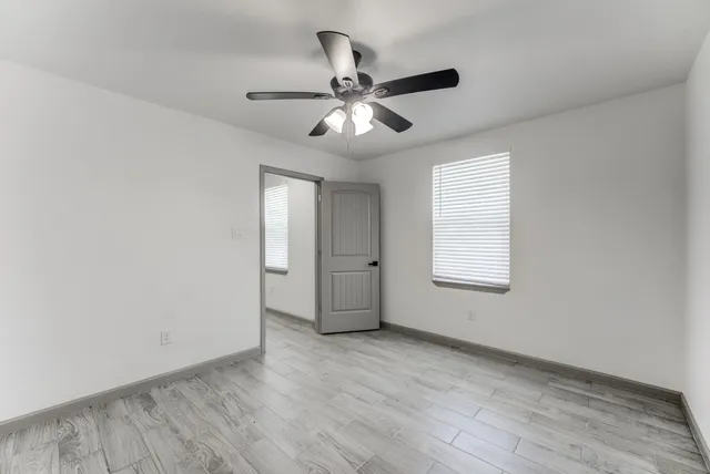 an empty room with wooden floor ceiling fan and windows