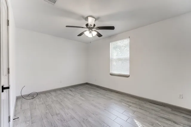 an empty room with wooden floor ceiling fan and windows
