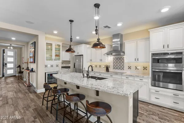 a kitchen with stainless steel appliances kitchen island granite countertop a stove a sink a oven a dining table and chairs with wooden floor