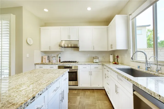 a large kitchen with stainless steel appliances granite countertop a stove a sink a refrigerator and white cabinets with wooden floor