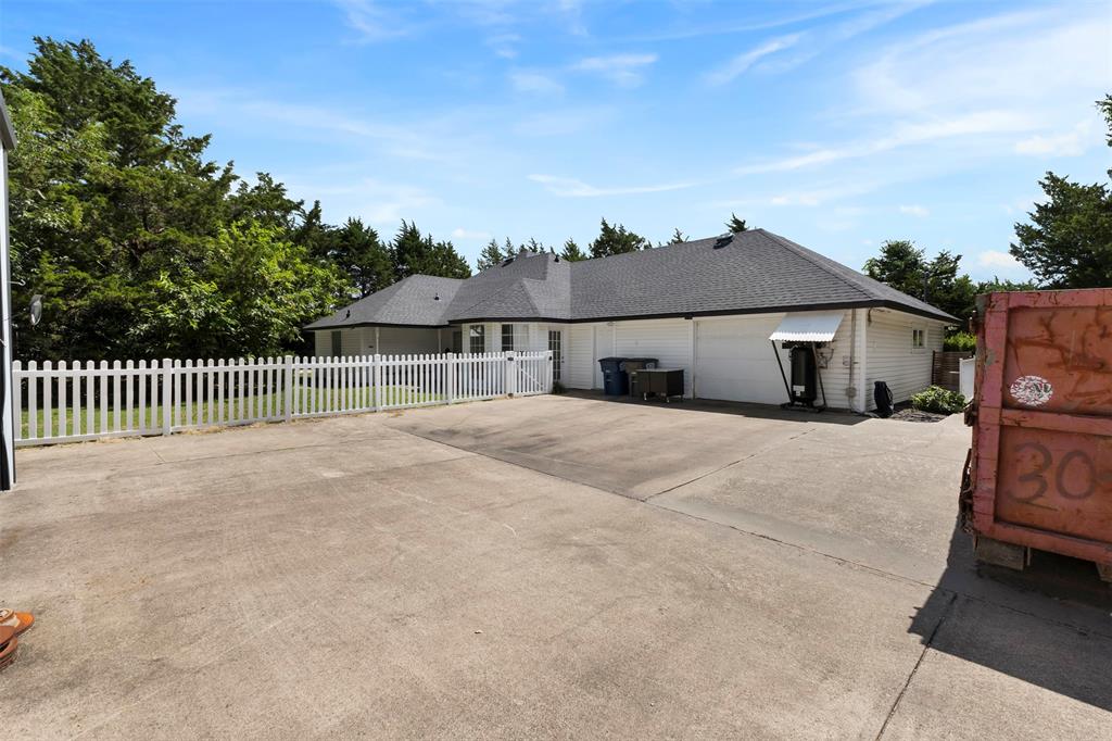 401 Rugged Drive Red Oak, TX 75154 - Photo 34 of 40 Spacious concrete driveway with a white picket fence, leading to a single-story home featuring a dark shingle roof and white siding