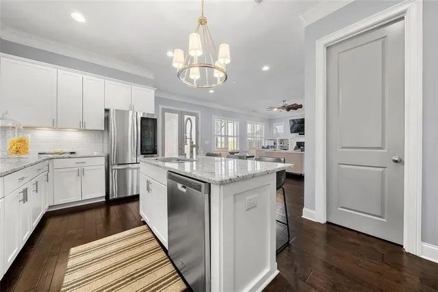 a kitchen with stainless steel appliances granite countertop a refrigerator a sink dishwasher a stove and white cabinets with wooden floor