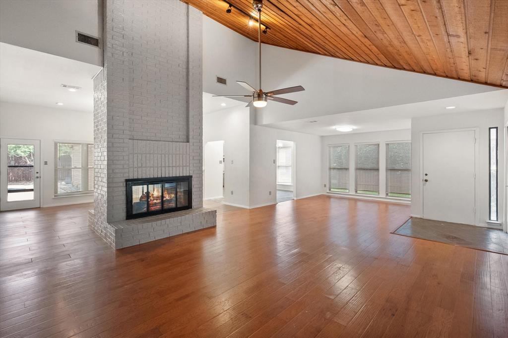 1036 Clinton Street Carrollton, TX 75007 - Photo 5 of 40 Unfurnished living room with high vaulted ceiling, hardwood / wood-style flooring, a brick fireplace, plenty of natural light, and wooden ceiling
