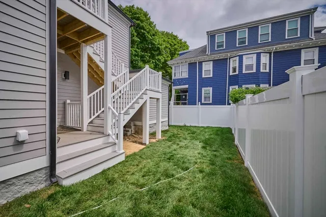 a view of a brick house with a small yard plants and wooden fence