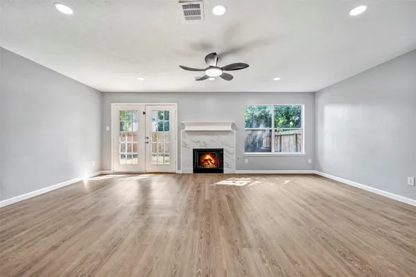 an empty room with wooden floor fireplace cabinet and windows