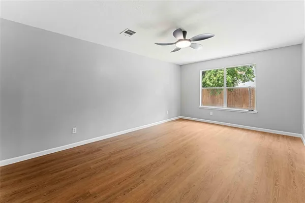 an empty room with wooden floor chandelier fan and windows