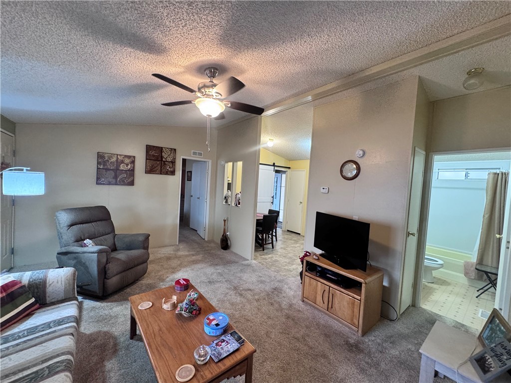 2532 Morgan Road Fort Mohave, AZ 86426 - Photo 13 of 29 Living room featuring a barn door, carpet flooring, vaulted ceiling, a textured ceiling, and a ceiling fan