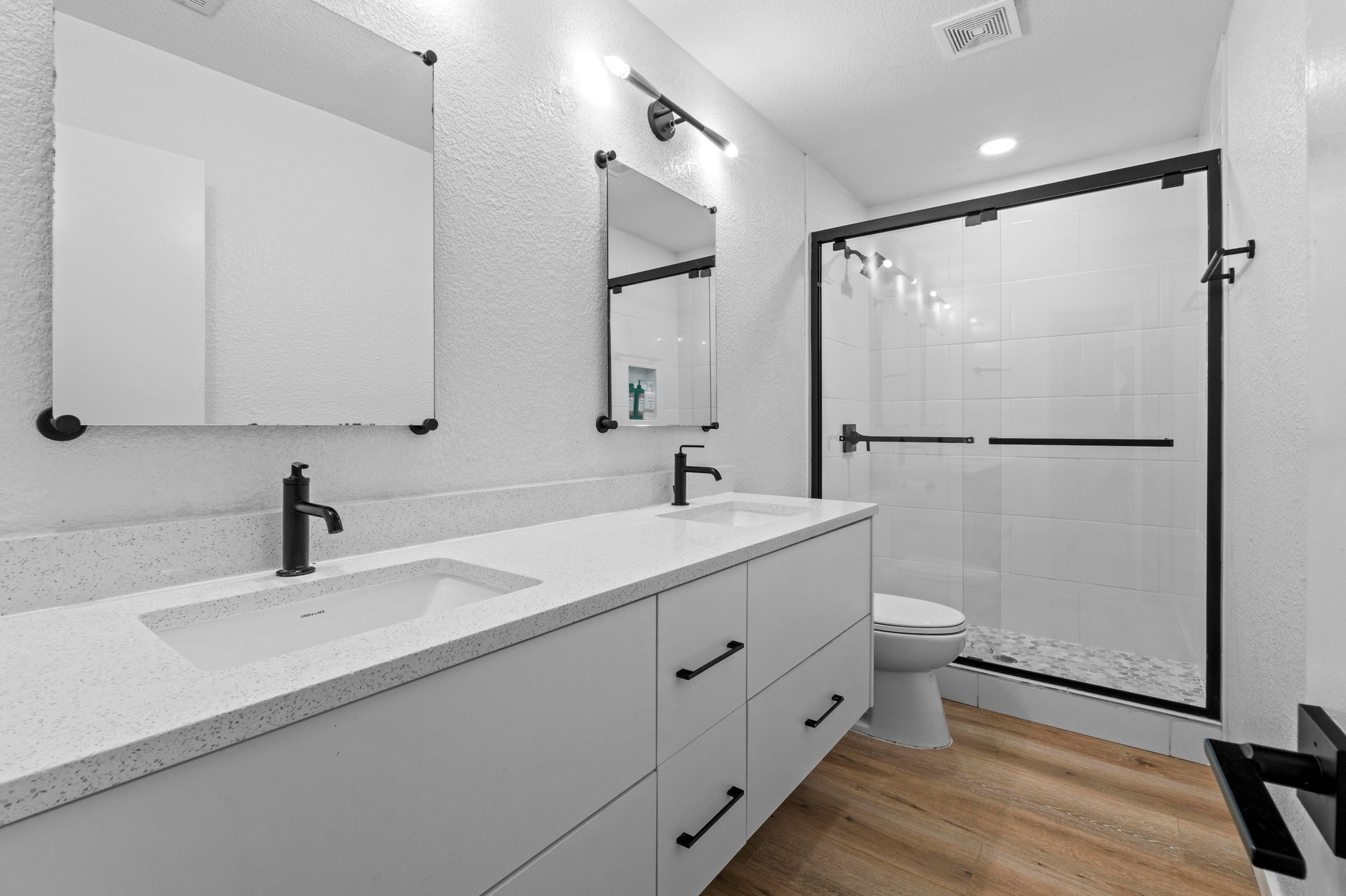 10601 Macmora Road, Unit B Austin, TX 78758 - Photo 14 of 22 Dual vanity sinks complement the modern, white-tiled shower with sleek black fixtures, creating a serene and functional bathroom.