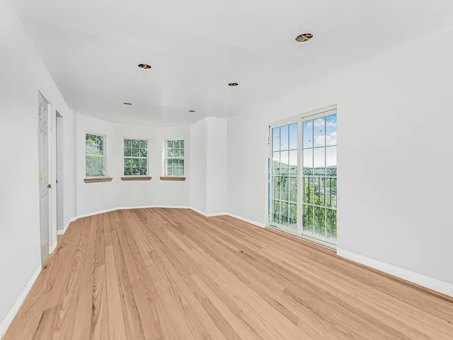 a view of an empty room with a window and wooden floor