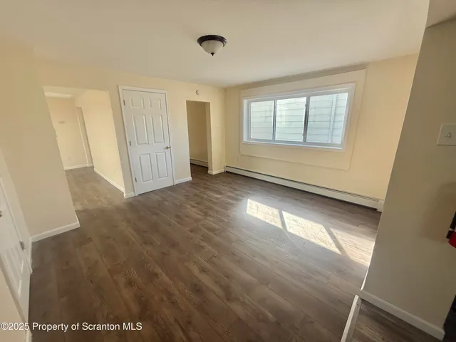 a view of an empty room with wooden floor and a window