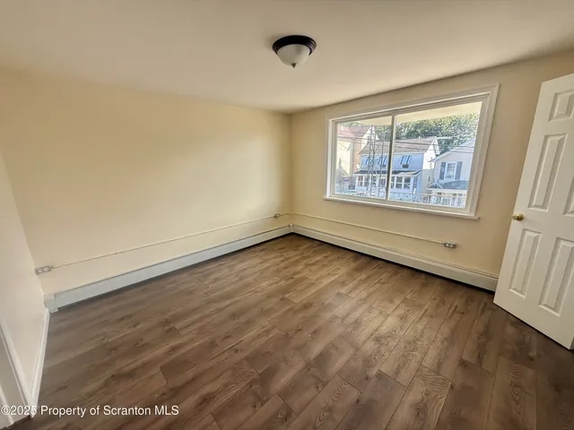 a view of an empty room with a window and wooden floor