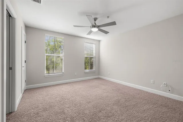 an empty room with ceiling fan and windows