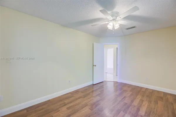 a view of an empty room with wooden floor and a ceiling fan