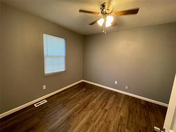 an empty room with wooden floor fan and windows