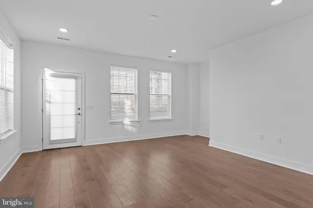 an empty room with wooden floor and windows with curtains
