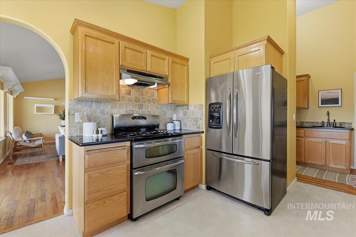 7900 Labor Camp Road Caldwell, ID 83607 - Photo 12 of 45 Stainless steel appliances, wood-finish cabinetry, black countertops, tile backsplash, and a large window