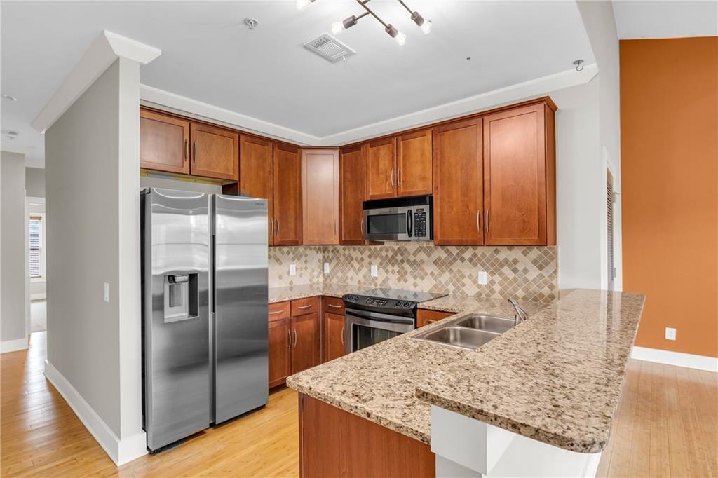 a kitchen with stainless steel appliances granite countertop a refrigerator a stove and a sink with wooden floor