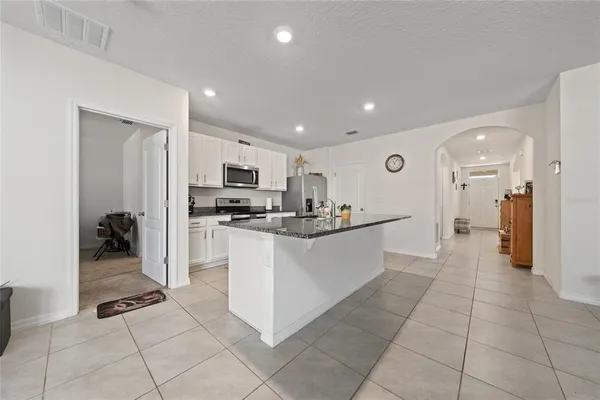 a large white kitchen with stainless steel appliances kitchen island granite countertop a refrigerator and a sink