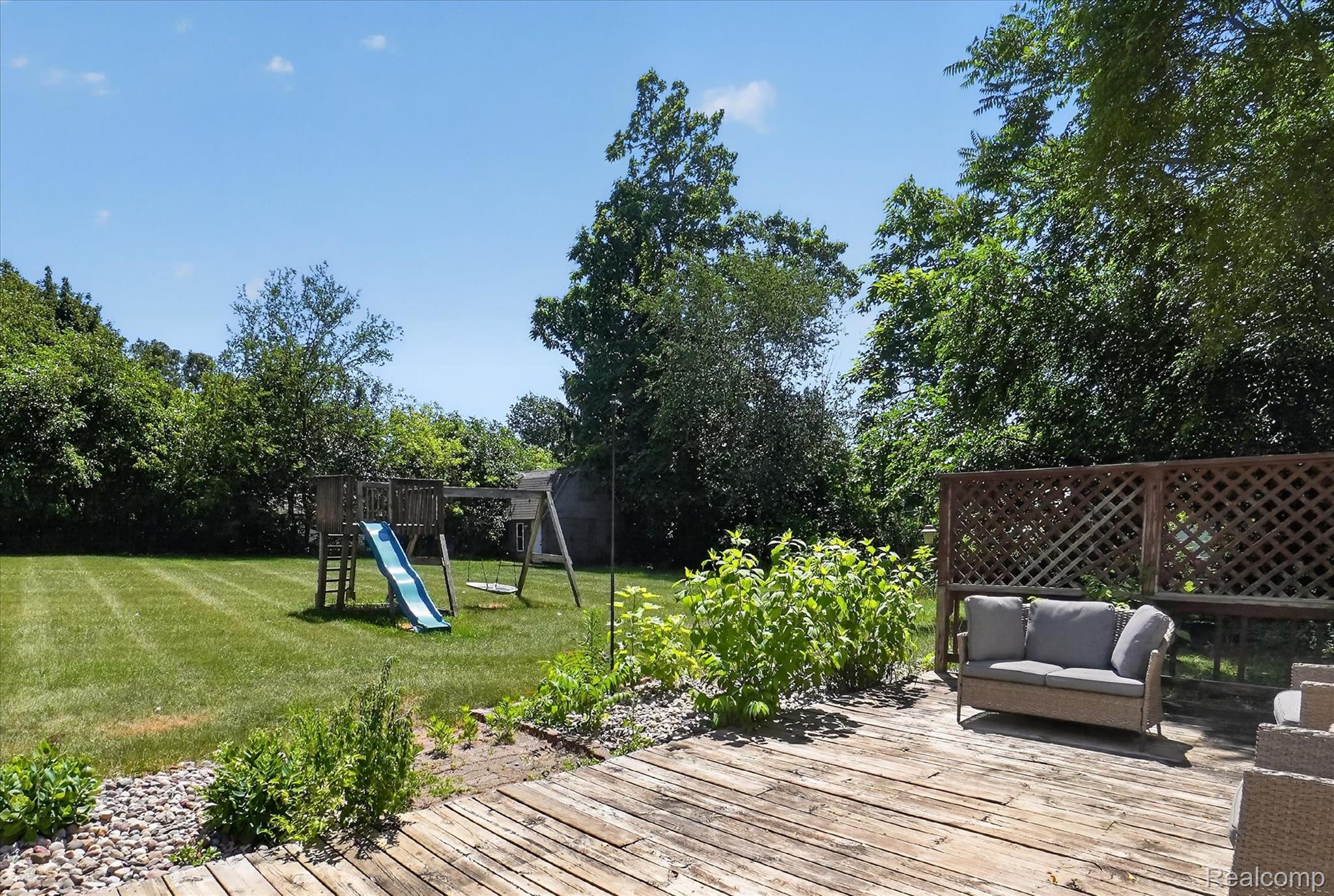 508 Deland Road Flushing, MI 48433 - Photo 35 of 38 Spacious backyard featuring a wooden deck, lattice privacy screen, and a large grassy area surrounded by mature trees