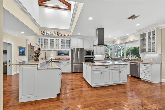 a kitchen with stainless steel appliances kitchen island granite countertop a refrigerator oven stove a sink dishwasher and white cabinets with wooden floor