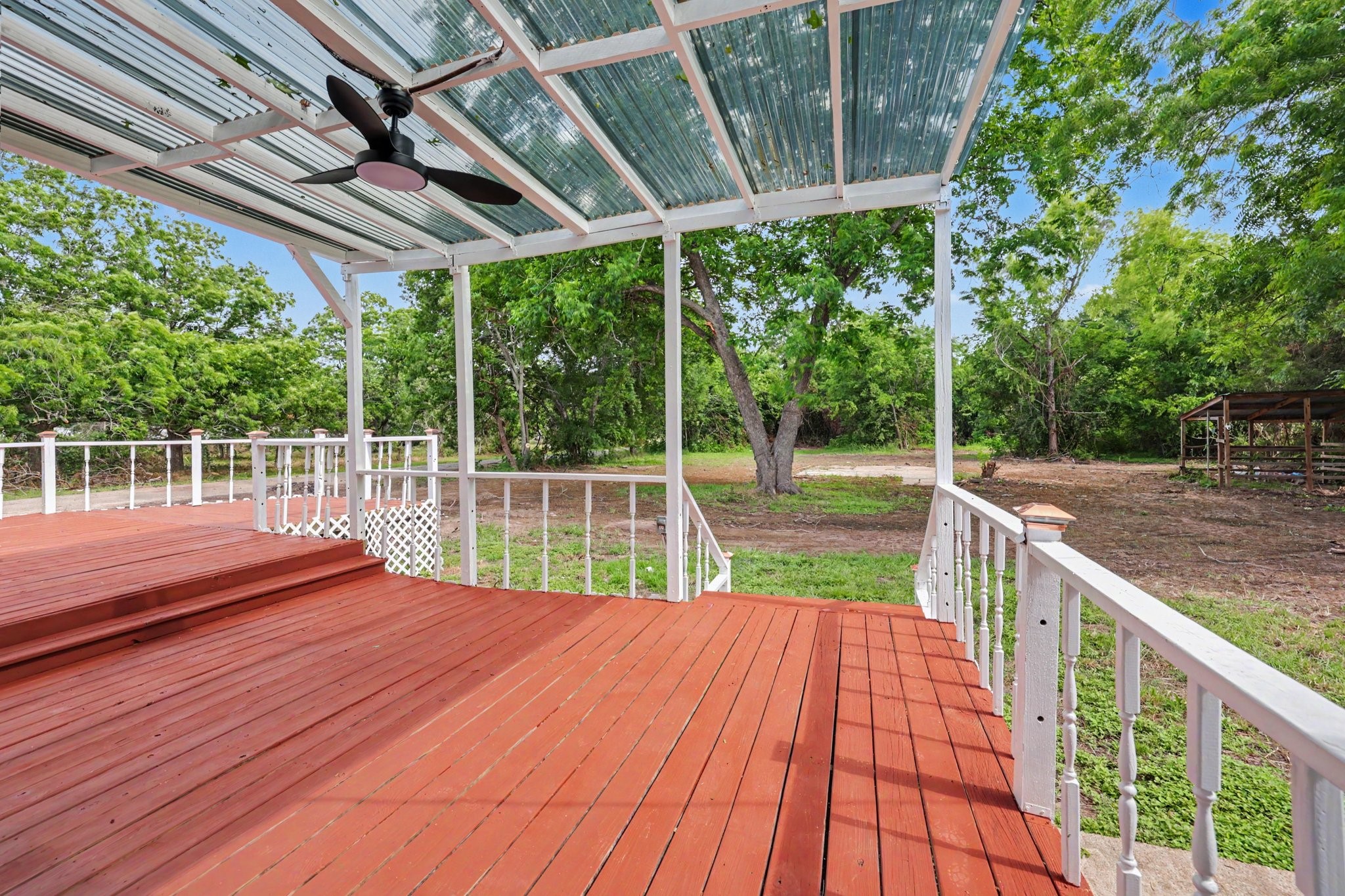 31730 Waller Tomball Road Waller, TX 77484 - Photo 40 of 50 Spacious wooden deck with a corrugated roof and ceiling fan, offering a comfortable outdoor area. The deck is surrounded by lush greenery, providing a serene and private setting.