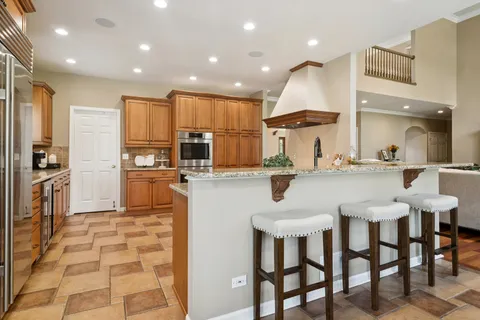 a kitchen with stainless steel appliances kitchen island granite countertop a dining table chairs sink and cabinets